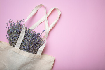 Lavender flowers bouquet in beige eco linen shopper bag on purple background top view. Romantic spring or summer girly feminine background, space for text.