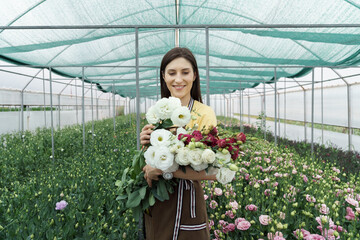 Woman florist has an order for fresh flowers. She makes a beautiful bouquet in the green house.