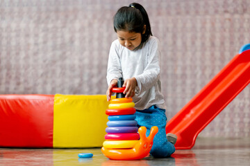 Niña latina feliz  jugando con pequeña torre de aros de colores. Entretenimiento interior....