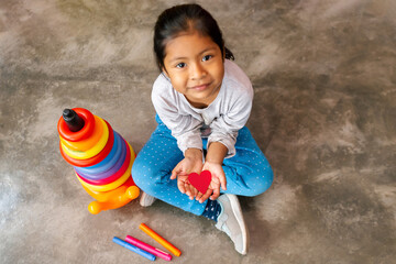 Naklejka premium Niña latina sonriente y feliz sosteniendo en sus manos un corazón de papel. Concepto de amor, Esperanza y felicidad. Espacio para texto.