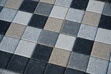 Checkered mosaic, multicolored paving slabs in closeup in gray and beige tones.