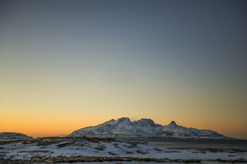 Fototapeta na wymiar Landscape shot highlighting the rugged mountains and snow-covered beaches of arctic norway during a brief golden hour during the long winters.