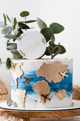 Birthday cake decorated with golden world map and flying airplane silhouettes on the white background. Traveling around the world concept. Birthday present for a traveller