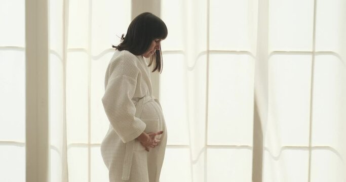 Pregnant woman experiences contractions and calmly walks around her bedroom during labor. Despite the discomfort of contractions, her determination and strength are evident in each step she takes.