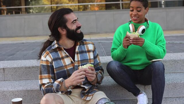 multiracial couple eating a sandwich outdoors in the street