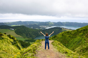 Young woman with open arms enjoying the freedom and the beautiful landscape view of the Twin Lakes in Sete Cidades in the island of Sao Miguel, Azores, Portugal