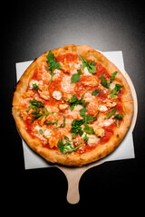Delicious Italian pizza with tomato sauce, arugula, soft cheese and smoked chicken pieces on wooden board on black surface