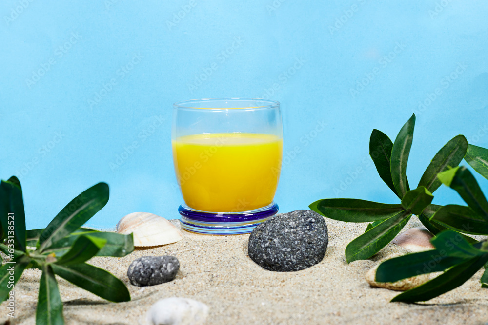 Wall mural glass of 100% orange juice on sand with stones and plants. summer concept