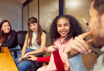 group of young multiracial college students or colleagues sitting indoors chatting interacting
