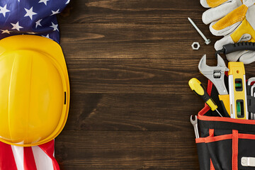 Engage your audience with a construction-themed Labor Day event. Top view shot of USA flag, set of tools, safety helmet, gloves on brown wooden background with empty space for advert or text - Powered by Adobe