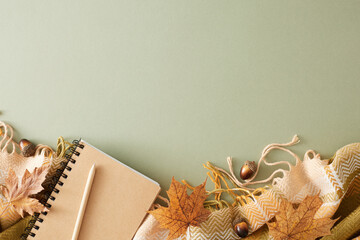 Immerse yourself in the comforts of fall at home. Top view composition of warm plaid, notebook, pen, acorns, yellow autumn leaves on pastel olive background with empty space for promo or text