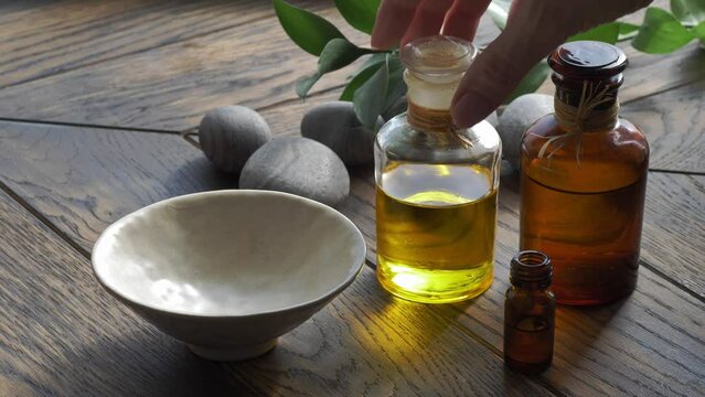 Base oil pouring from bottle to bowl on wooden background with stones and leaves