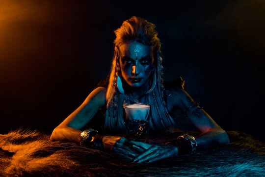 Photo of mysterious viking mythology wizard woman hold elixir cup yellow lights isolated on black color background