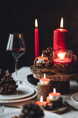 Rustic table decor for Christmas or New Year family dinner. Centrepiece with red candle, dry orange, cone, cinnamon, anise. Zero waste eco-friendly home. Cozy atmosphere, dark background. Close up