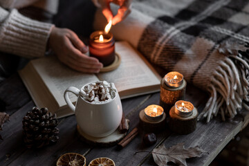 Aromatherapy on a grey fall morning, atmosphere of cosiness and relax. Autumn cozy home composition with hot chocolate with marshmallow and candles. Wooden background, books, close up.