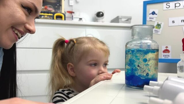 happy woman and girl look at the bottle with blue bubbles admiringly with a smile rejoicing spend time in laboratory for children chemical experiments interest learning physics chemistry preschool age