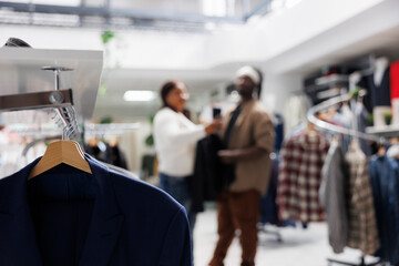 Clothes hanging on rack in store with bloggers taking selfie for brand promotion on blurred background. Casual apparel from new collection on hangers in fashion boutique close up selective focus