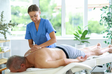 Female massage therapist working out back zone of male patient during deep tissue back massage