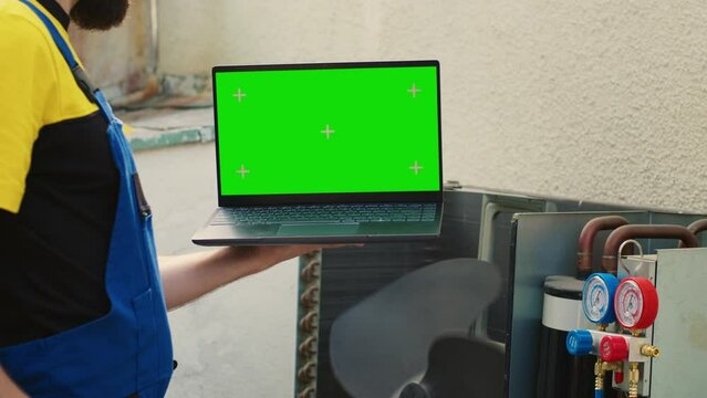 Experienced worker ordering new internal parts on green screen laptop for malfunctioning condenser after finishing review. Seasoned wireman looking online for air conditioner replacement components