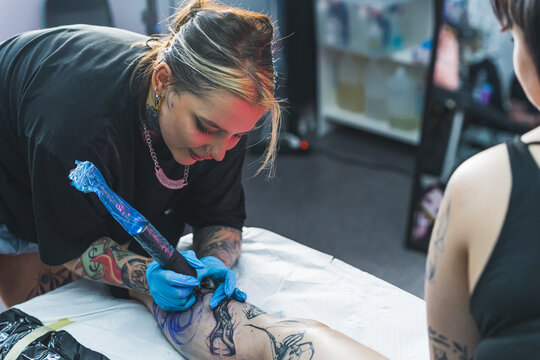 The long process of drawing a big leg tattoo. Indoor shot. Female tattooed artist using professional tattooing gun to draw a tattoo on her client's calf. High quality photo