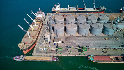 Loading grain into holds of sea cargo vessel in seaport from silos of grain storage. Bunkering of dry cargo ship with grain. Aerial top view