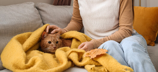 Woman with cute ginger cat in warm plaid at home on autumn day