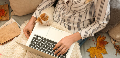 Woman with cute little kitten using laptop at home on autumn day