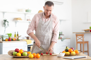 Mature man cutting strawberry for smoothie in kitchen