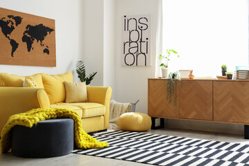 Interior of stylish living room with cozy yellow sofa and soft knitted blanket on pouf