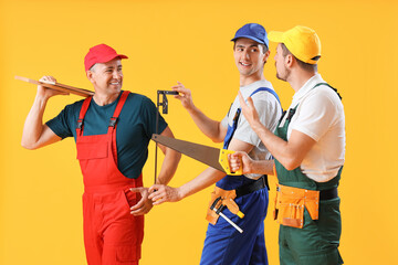 Team of male builders with tools on yellow background