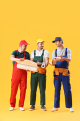 Team of male builders with wallpapers on yellow background