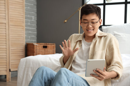 Young Asian man with tablet computer video chatting in bedroom