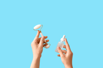 Woman with facial massage tool and cosmetic dropper bottle on blue background