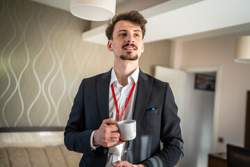 One man caucasian male adult stand with cup of coffee in hotel room