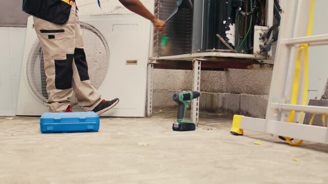 Ground level shot of trained engineer commissioned by home owner for yearly air conditioner routine maintenance, using soft dusting brush to clean dusty condenser coils and filters, outdoor