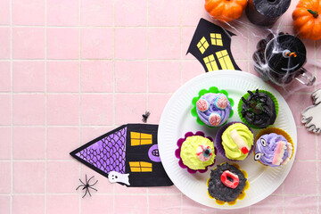 Fototapeta na wymiar Composition with delicious Halloween cupcakes and paper houses on pink tile background