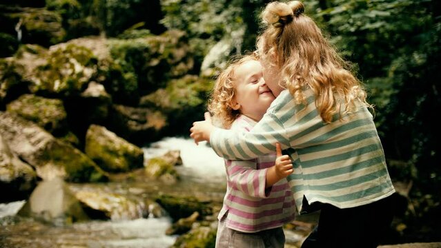 Little sisters hug each other at beautiful waterfall in the woods