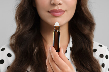 Woman with roller bottle of essential oil on light grey background, closeup