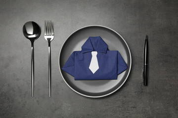 Plate with shirt made of paper napkin, cutlery and pen on gray table, flat lay. Business lunch...