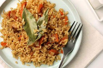 Delicious pilaf, bay leaves and fork on table, top view