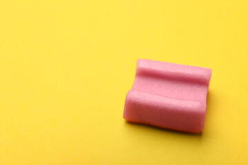 Tasty pink chewing gum on yellow background, closeup. Space for text