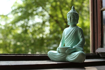 Decorative Buddha statue on wooden windowsill, space for text