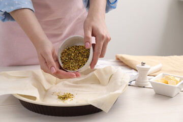 Woman putting filling into baking dish with dough to prepare baklava at white wooden table, closeup