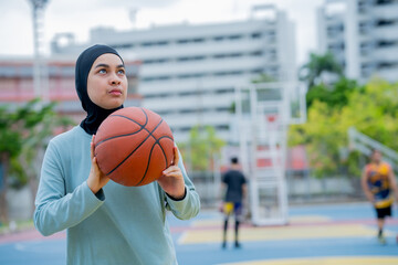 Young asian muslim girl teen wearing hijab going to play basketball on the outdoor court in the morning with determination, Muslim sport concept. © maya1313