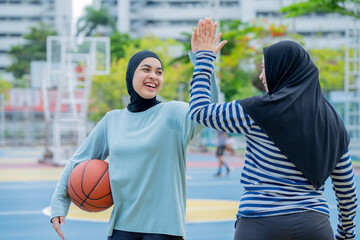 Young asian muslim girl teen wearing hijab going to play basketball on the outdoor court in the morning with determination, Muslim sport concept.