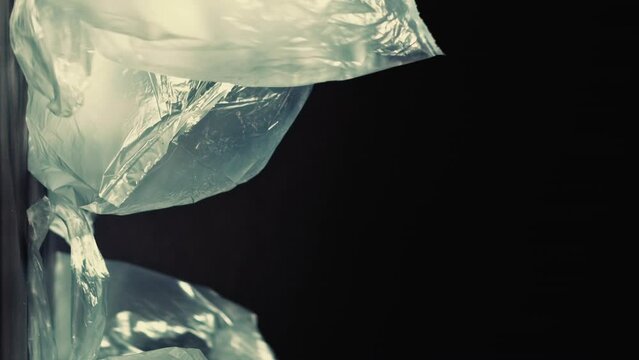Vertical video. Plastic contamination. Waste management. Stop pollution. Used blown cellophane bags falling in garbage pile isolated on dark background empty space.