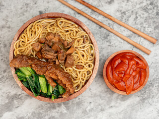 Indonesian chicken noodles called mie ayam topped with chicken meat and green mustard served in a bowl with red spicy sauce