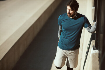 Young man stretching before jogging and exercising on a sidewalk on a bridge in the city