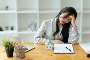 Tired house broker in stress works at a laptop while sitting at a table and holds her hand on her...
