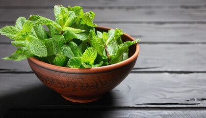 Clay bowl with a bunch of fresh mint on the black wooden table. The concept of healthy eating.